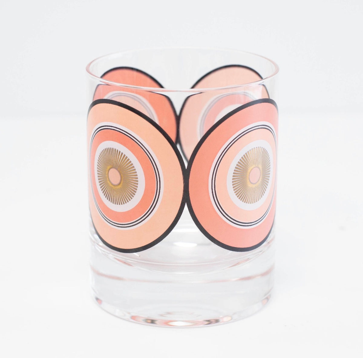 Angled view of vintage-inspired whiskey glass featuring repeating pink circles and metallic gold starburst details