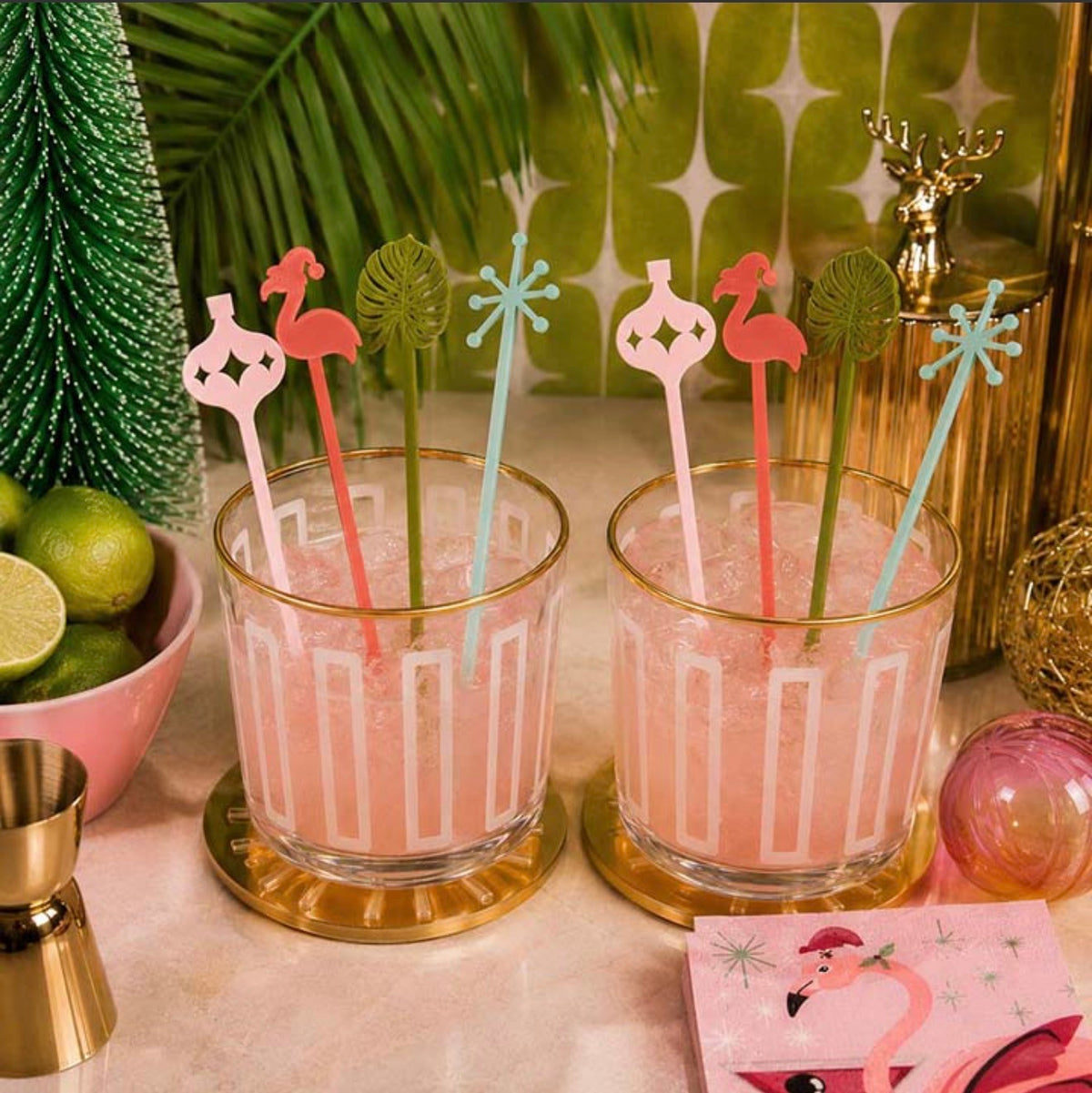 Pair of frosted geometric rocks glasses with gold rims styled with pink cocktails and colorful retro drink stirrers
