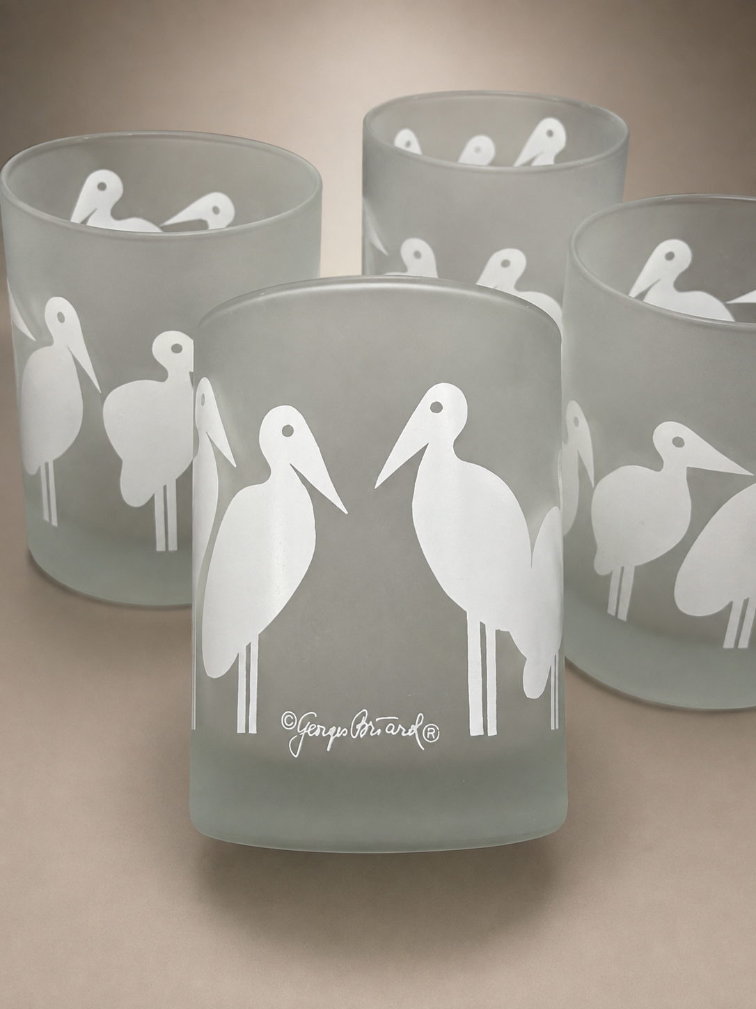 Four Georges Briard frosted old fashioned glasses displayed together showing the repeating bird pattern.