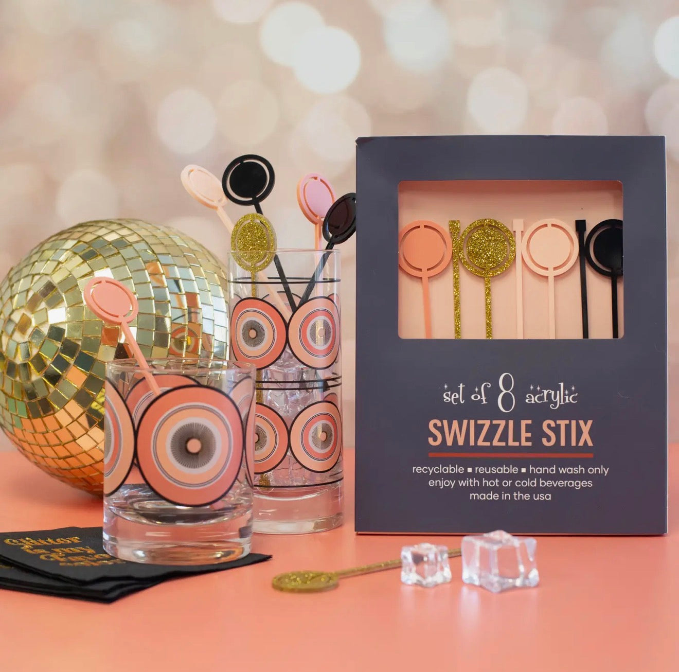 Pink and gold acrylic drink stirrers displayed in premium gift packaging alongside coordinating cocktail glasses.