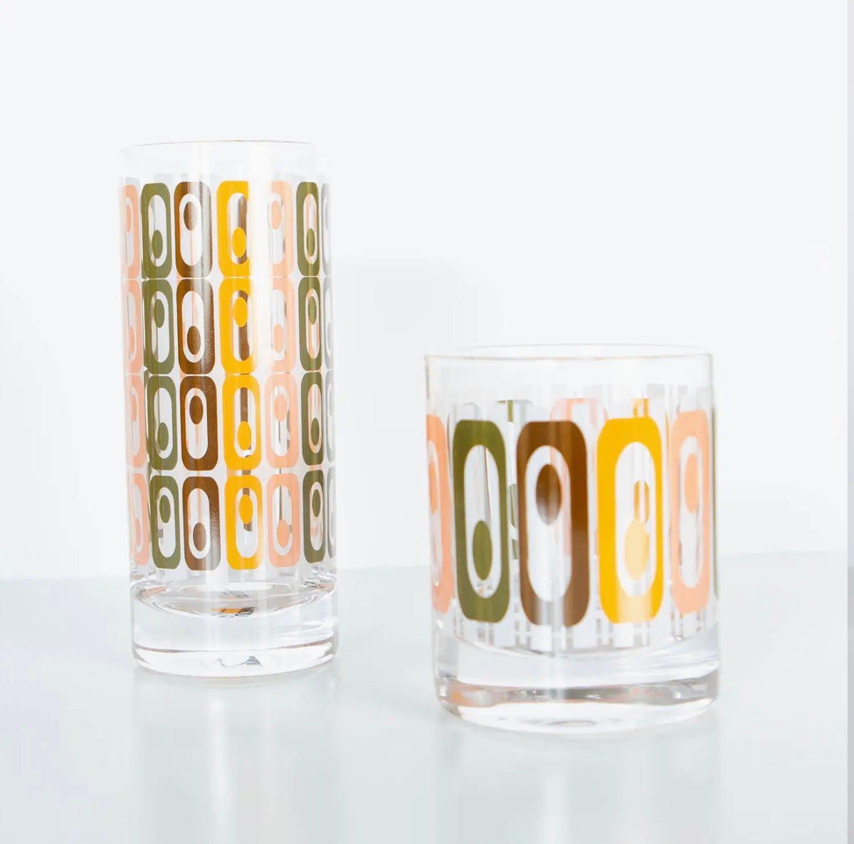 Vintage-inspired tiki whiskey rocks glass and coordinating highball featuring a retro geometric pattern in orange, peach, green and brown