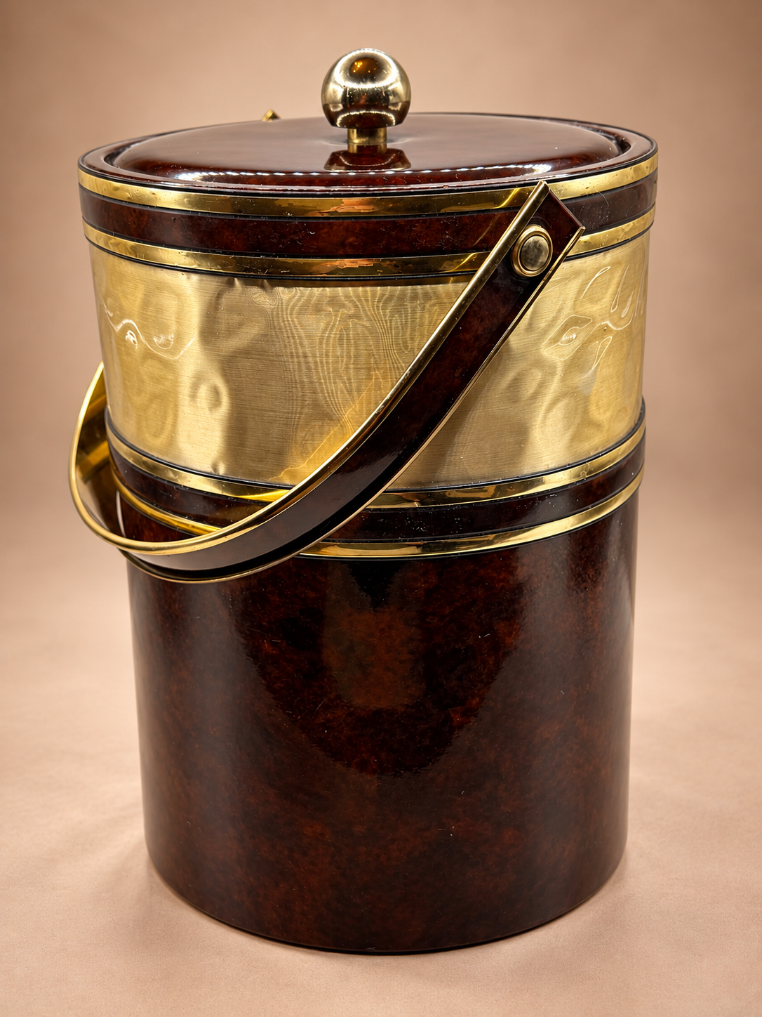 Angled view of vintage brown and gold insulated ice bucket with coordinating lid, gold finial and swing handle.