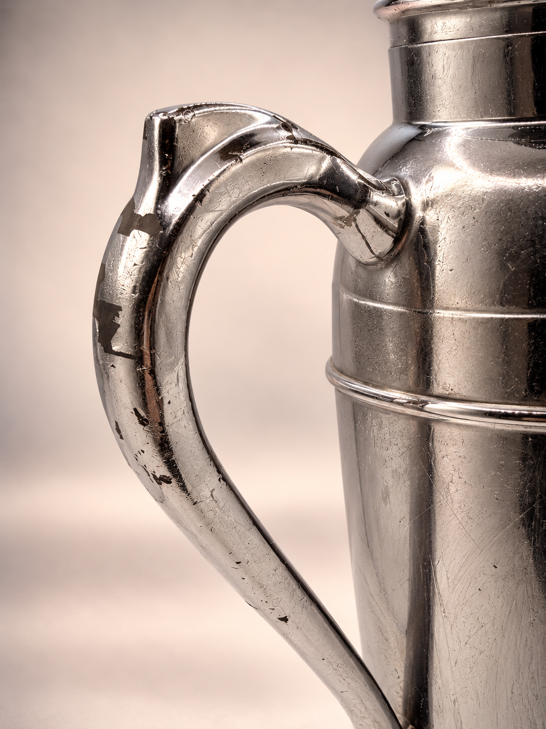 Detailed view of vintage cocktail shaker handle showing extensive finish loss, exposed darker underlying material, and scratches.