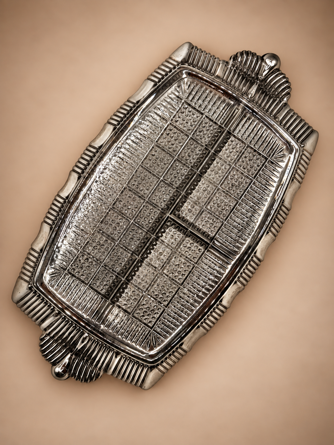 Underside of vintage three-compartment glass relish dish showing geometric pressed-glass texture and silver-tone trim.