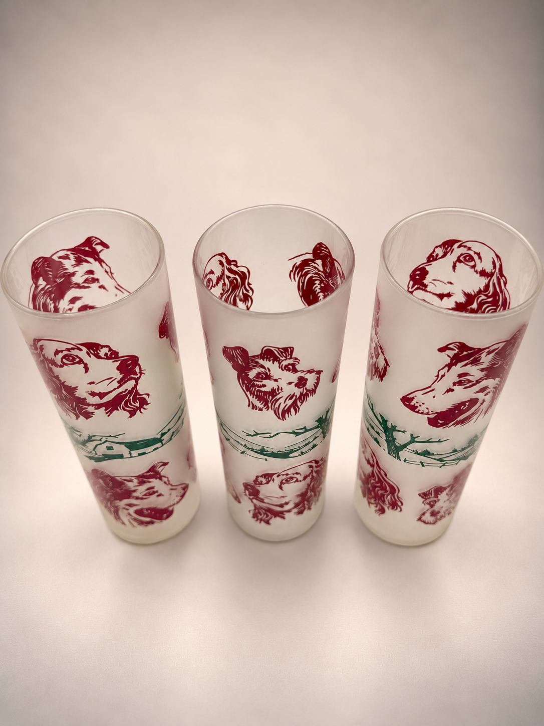 Elevated view of three vintage dog-themed drinking glasses showing their frosted interiors and wraparound canine illustrations.