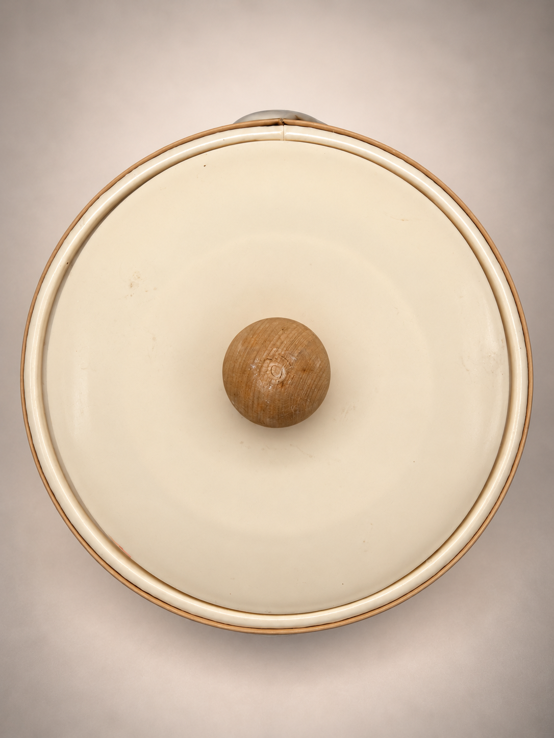 Overhead view of ivory-colored vintage ice bucket lid with natural wood ball knob and light surface marks.