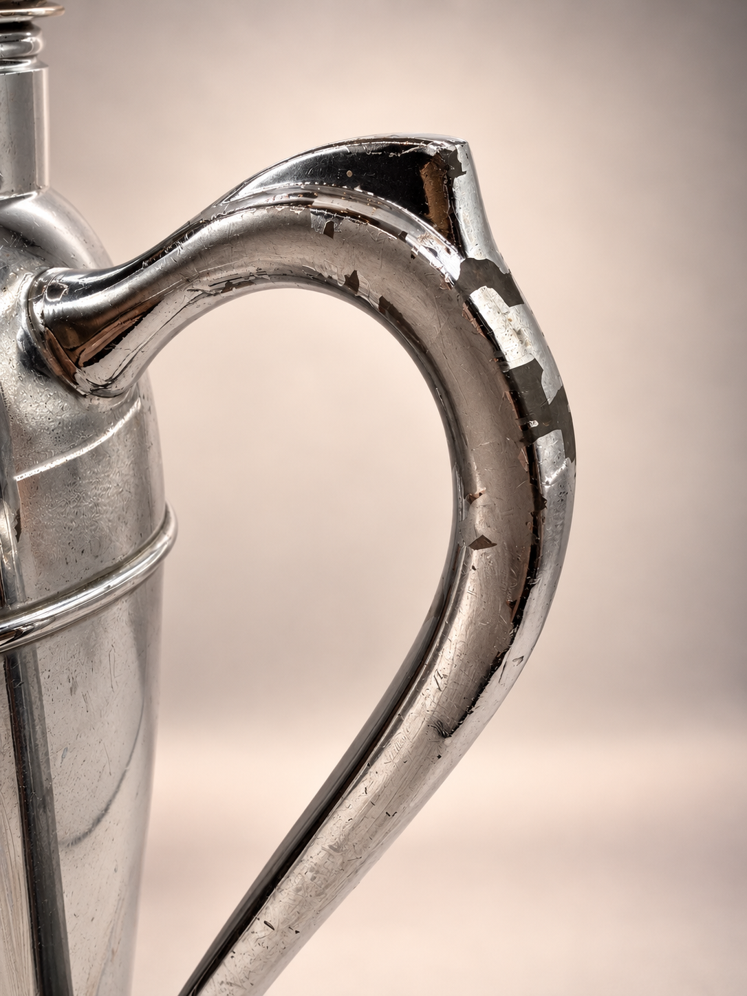 Close-up of curved cocktail shaker handle showing scratches and substantial areas of worn or missing silver-tone finish.