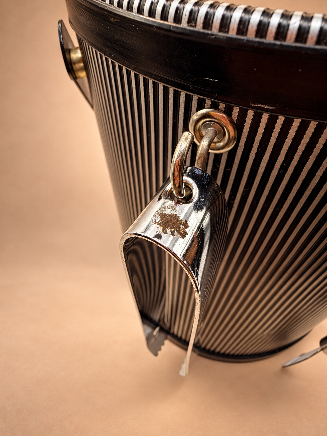Close-up showing age-related surface wear and finish loss on silver-tone tool attached to vintage striped ice bucket.