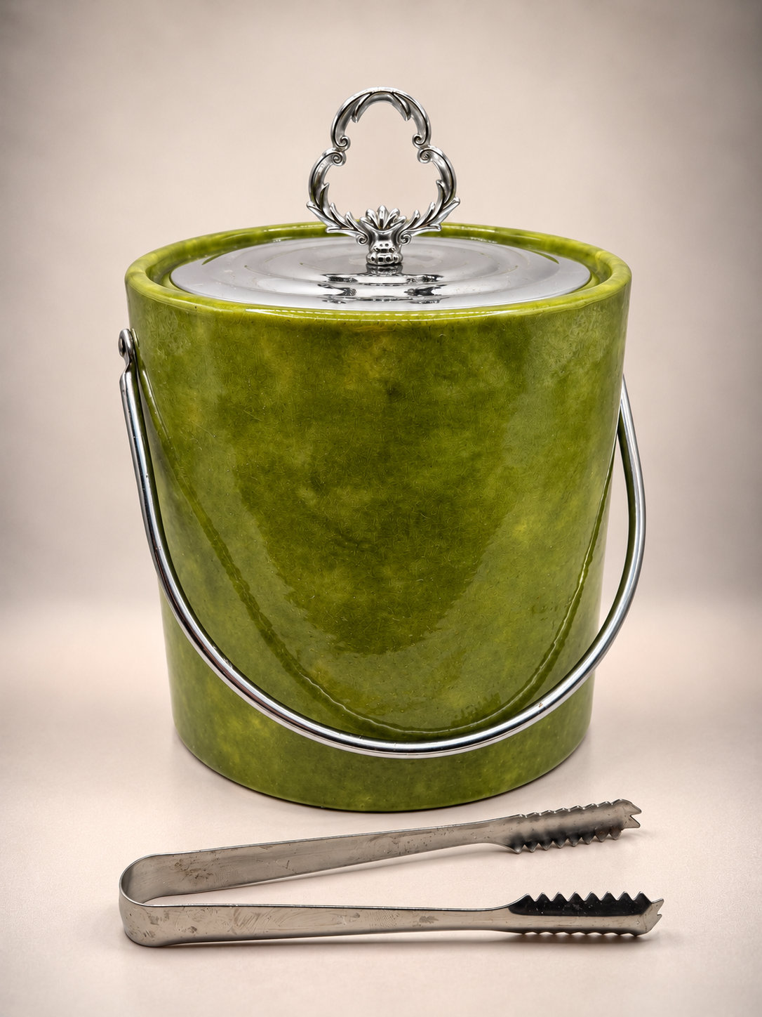 Vintage Irvinware olive-green ice bucket with ornate silver-tone lid, swing handle, and metal ice tongs displayed in front.