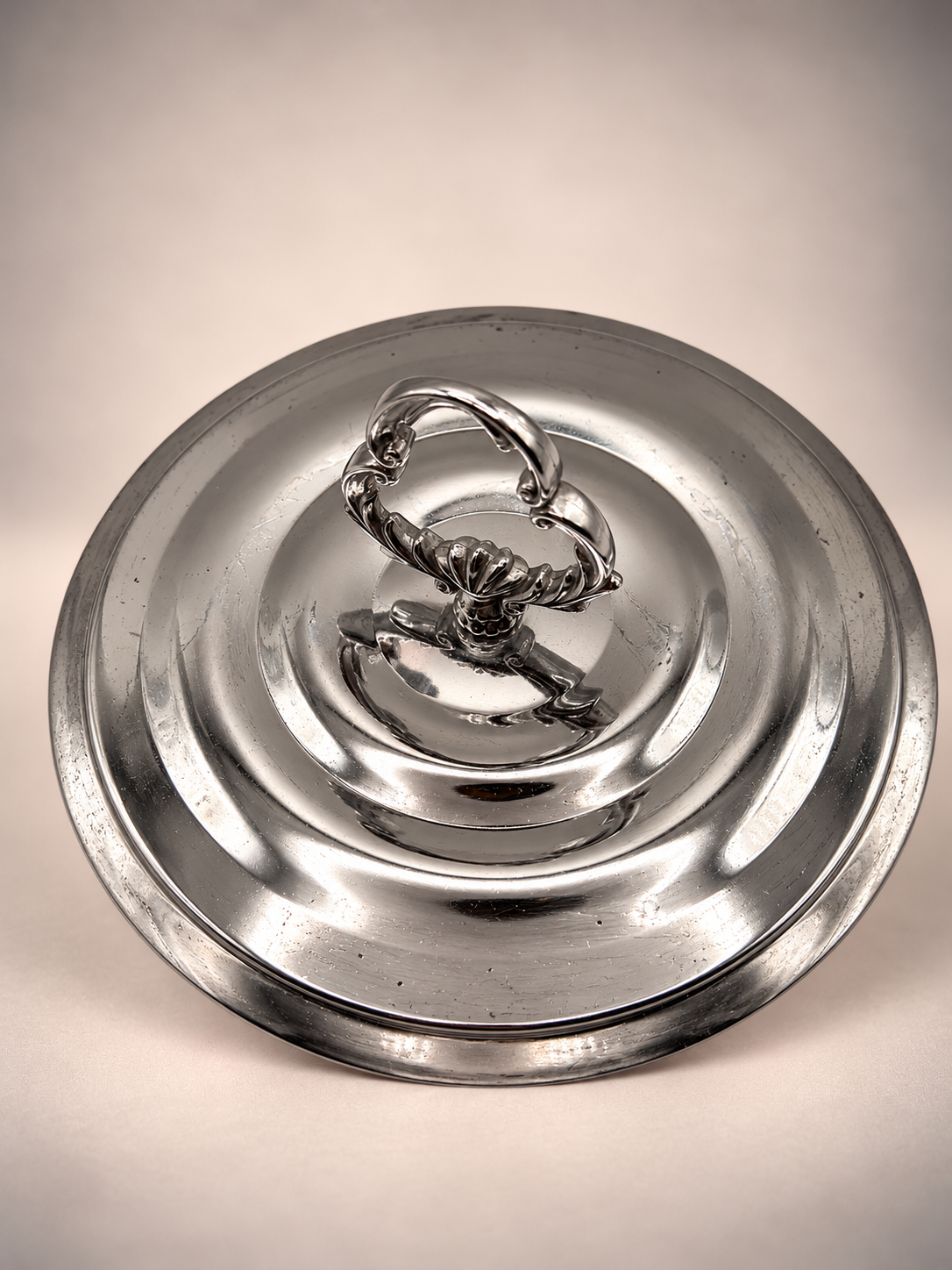 Overhead view of silver-tone ice bucket lid showing ornate handle, circular design, scratches, and vintage surface wear.