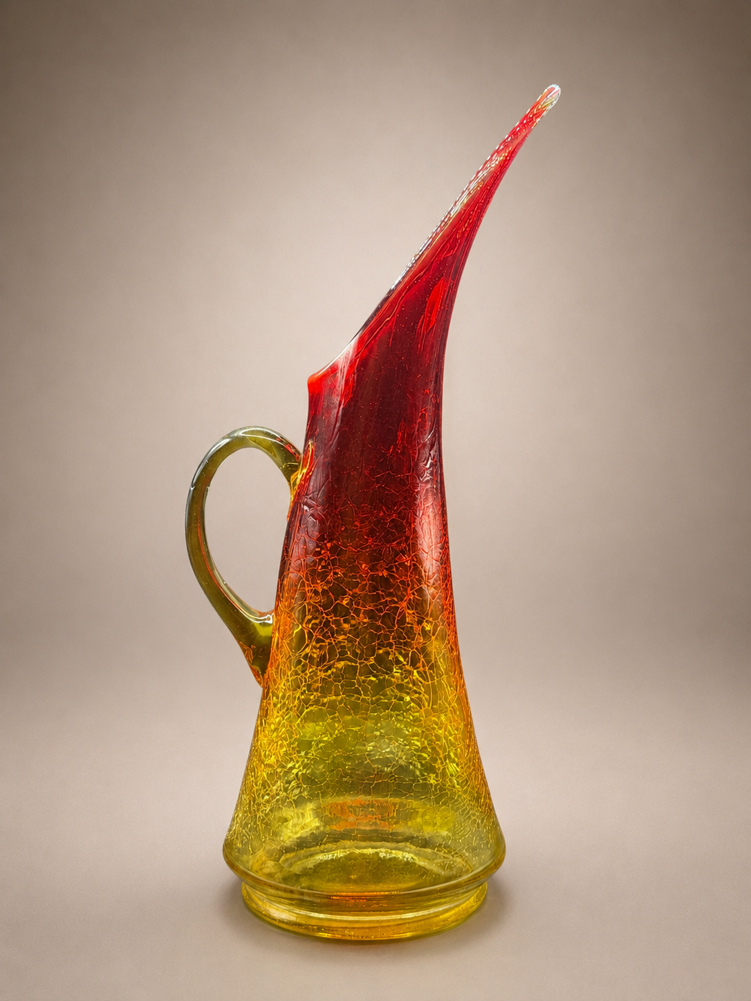 Front view of a vintage Kanawha Glass Amberina crackle glass pitcher featuring a dramatic swung spout and applied green handle.