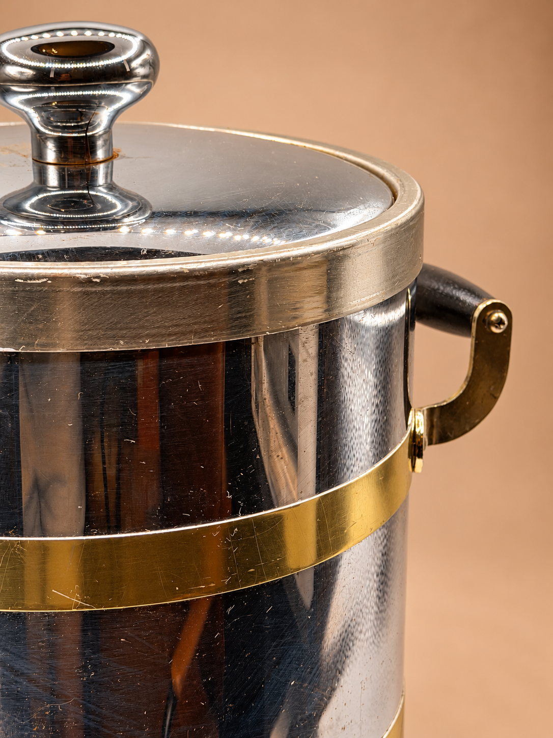 Close-up of vintage Kraftware ice bucket showing reflective silver finish, gold-tone band, upper rim and side handle.