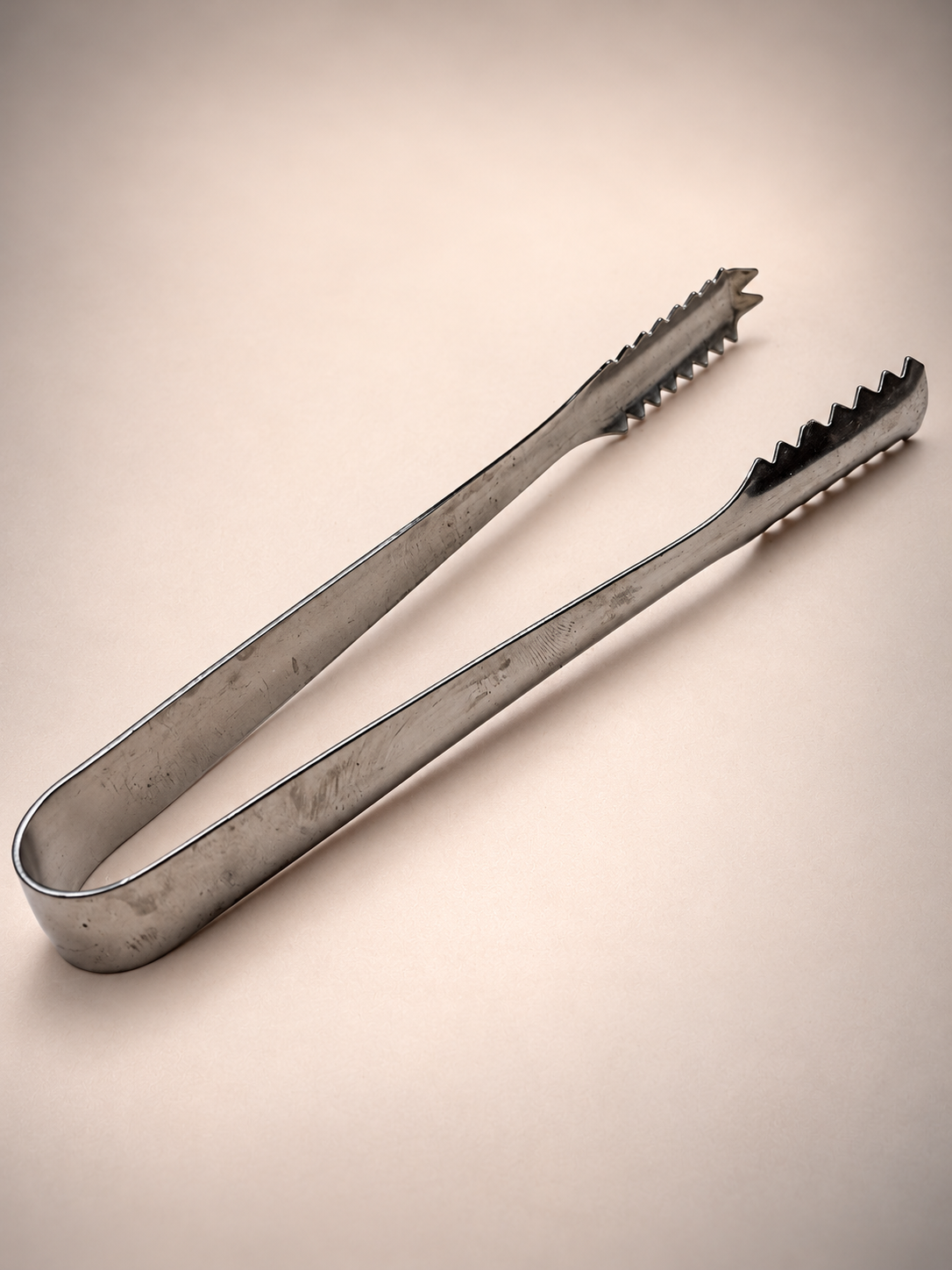 Close-up of vintage silver-tone ice tongs showing serrated gripping ends and cosmetic wear from previous use.