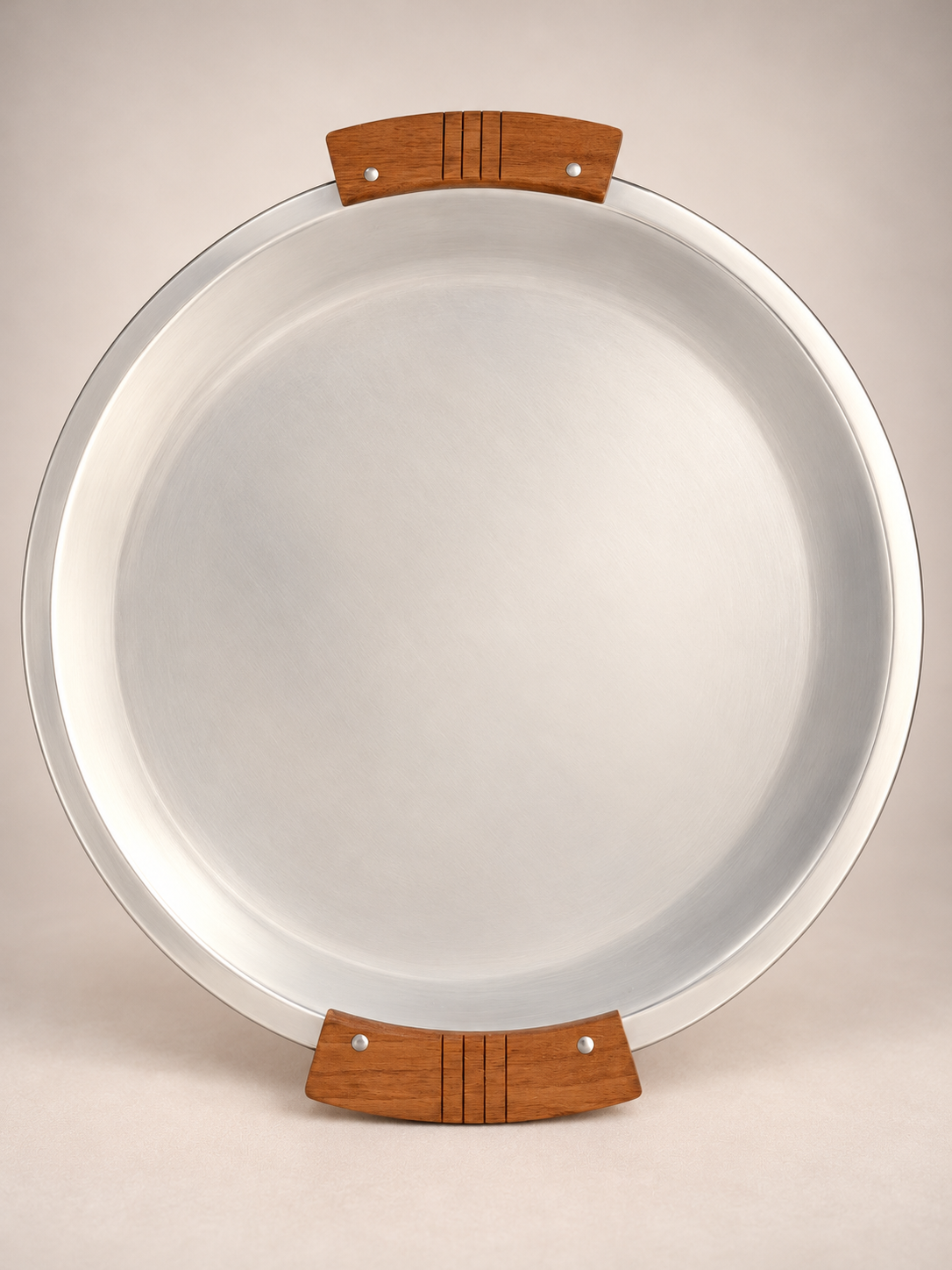 Overhead view of a vintage round silver-tone metal serving tray with two curved wooden handles featuring decorative grooves.