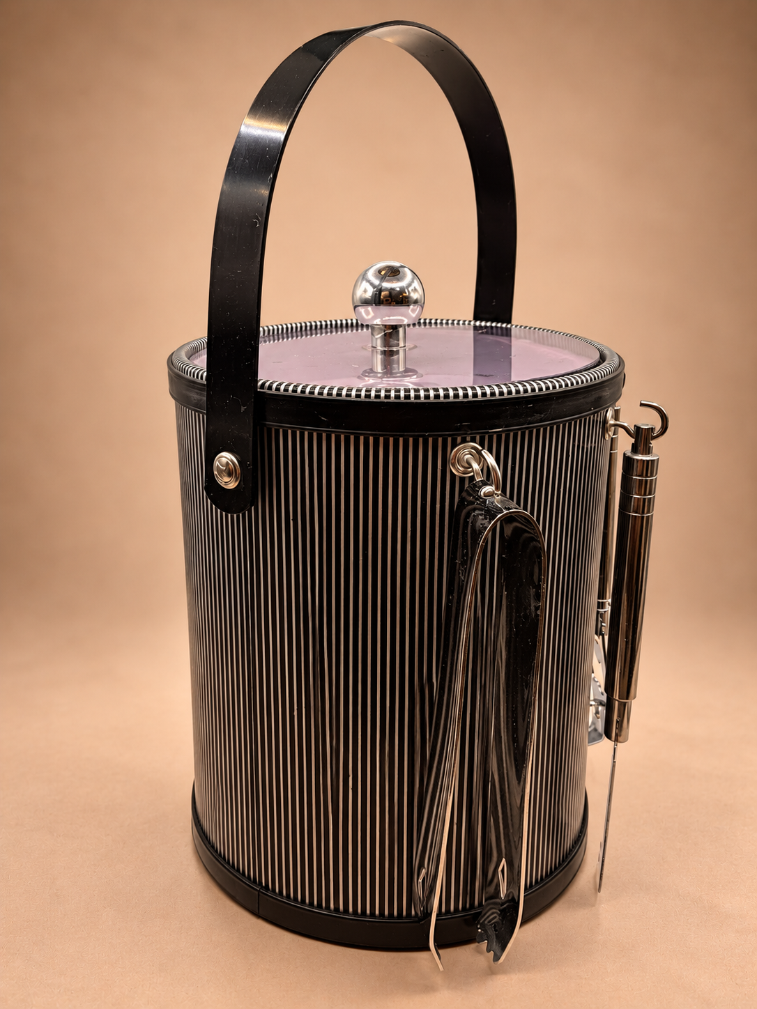 Side view of vintage black and silver striped ice bucket showing swing handle, translucent lid and hanging bar tools.