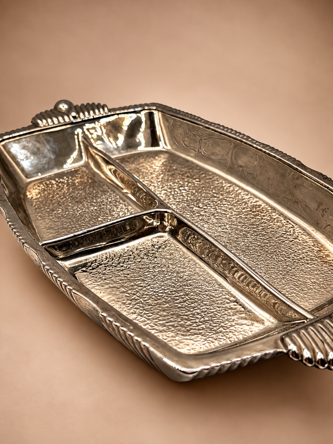 Low-angle view of vintage three-section glass relish dish showing textured compartments and reflective silver-tone sides.