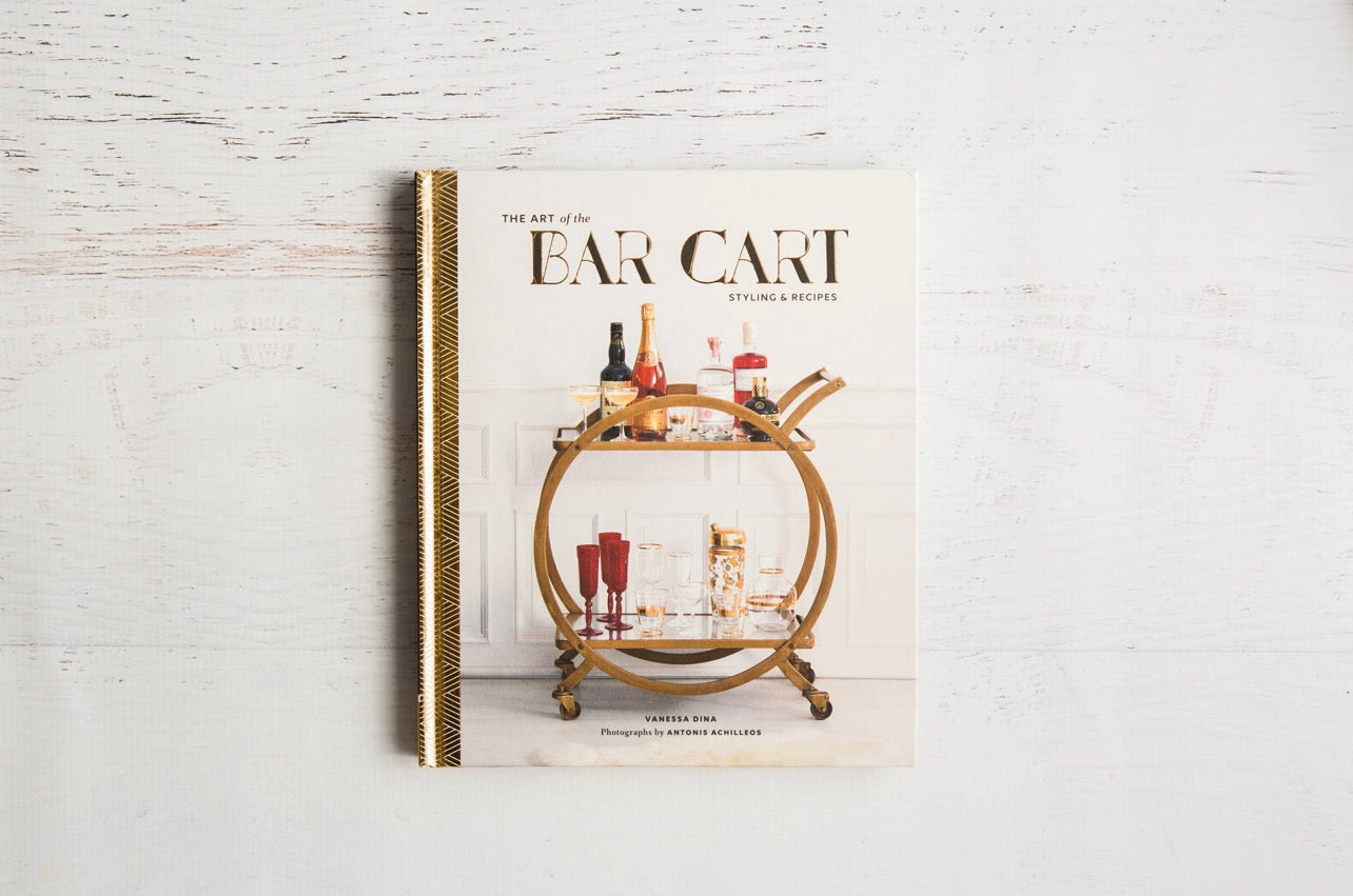 Flat lay of The Art of the Bar Cart book on a light wood surface, featuring a styled bar cart cover—an elegant gift for cocktail lovers.