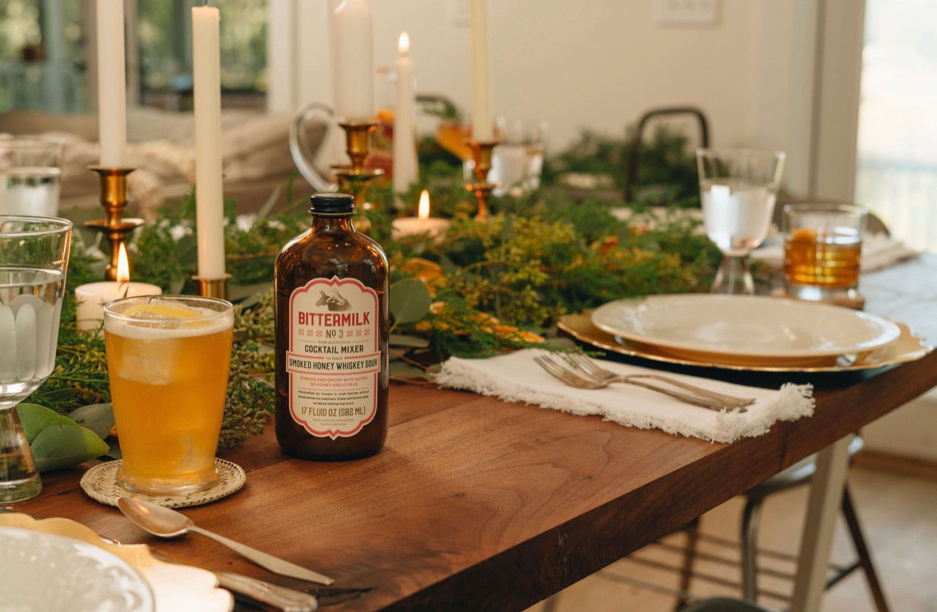 Bittermilk whiskey sour mixer on styled dining table with cocktail glass candles and greenery for entertaining