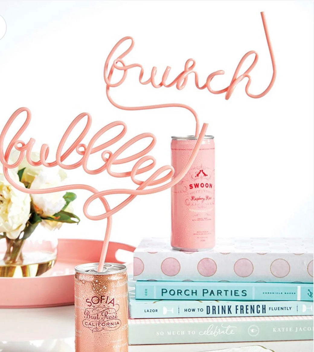 Pink bubbly script novelty straw displayed in sparkling wine cans with party books and pink decor