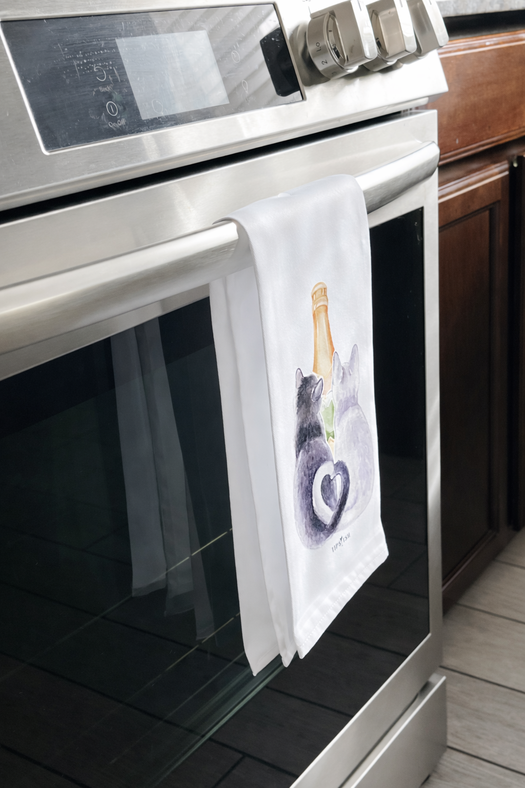 Cat themed champagne kitchen towel hanging on oven handle in modern kitchen