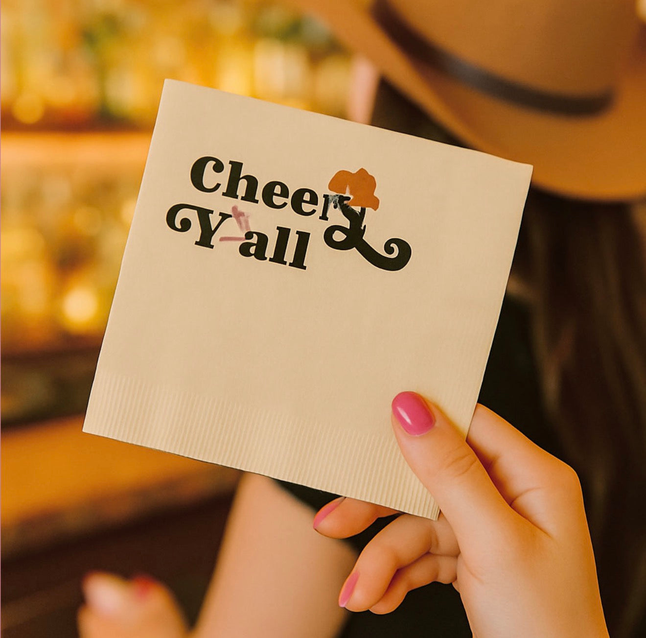 Woman holding Cheers Y’all western cocktail napkin at country themed party