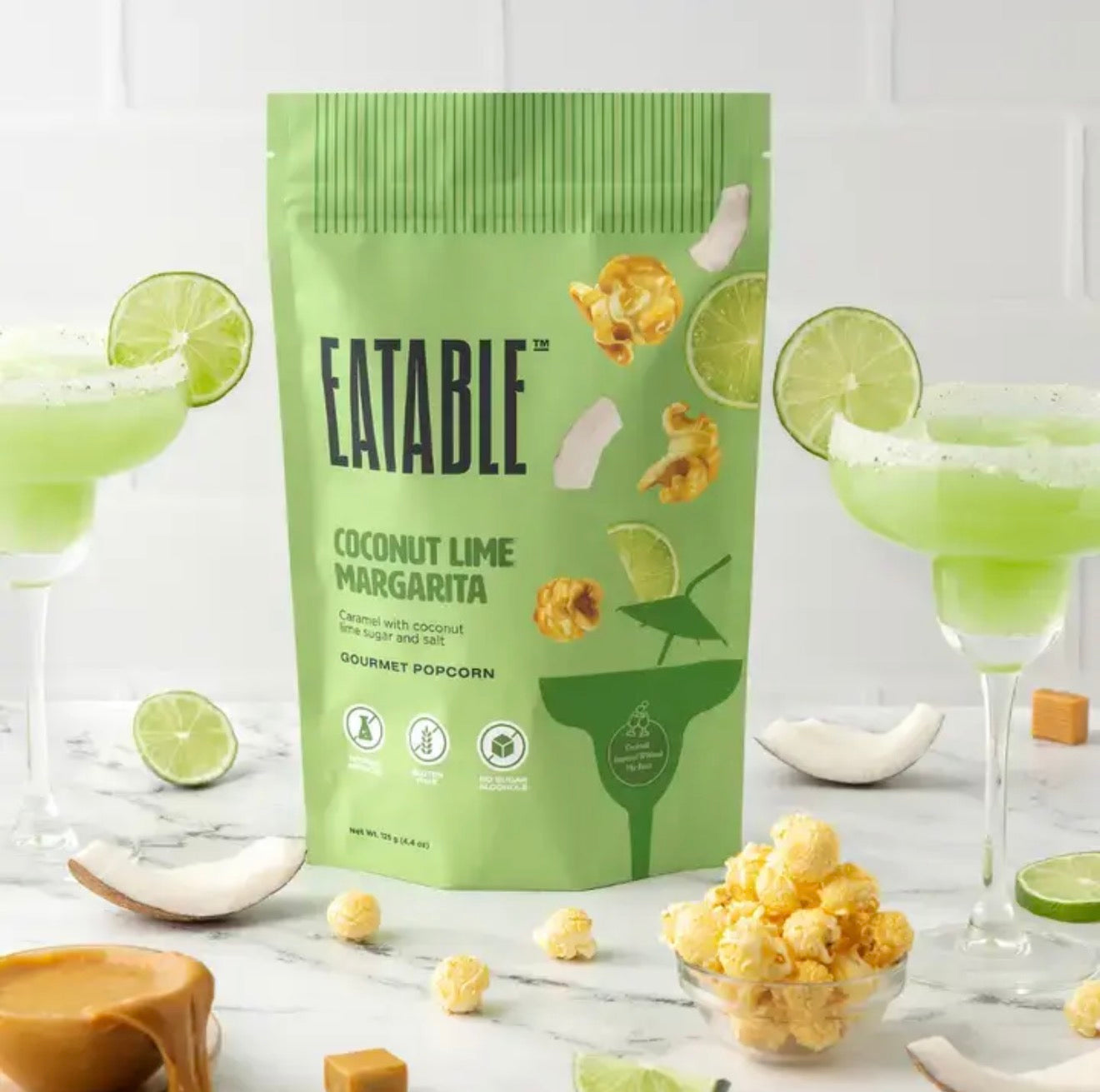 Eatable Coconut Lime Margarita gourmet popcorn bag styled with margarita glasses, limes, and coconut