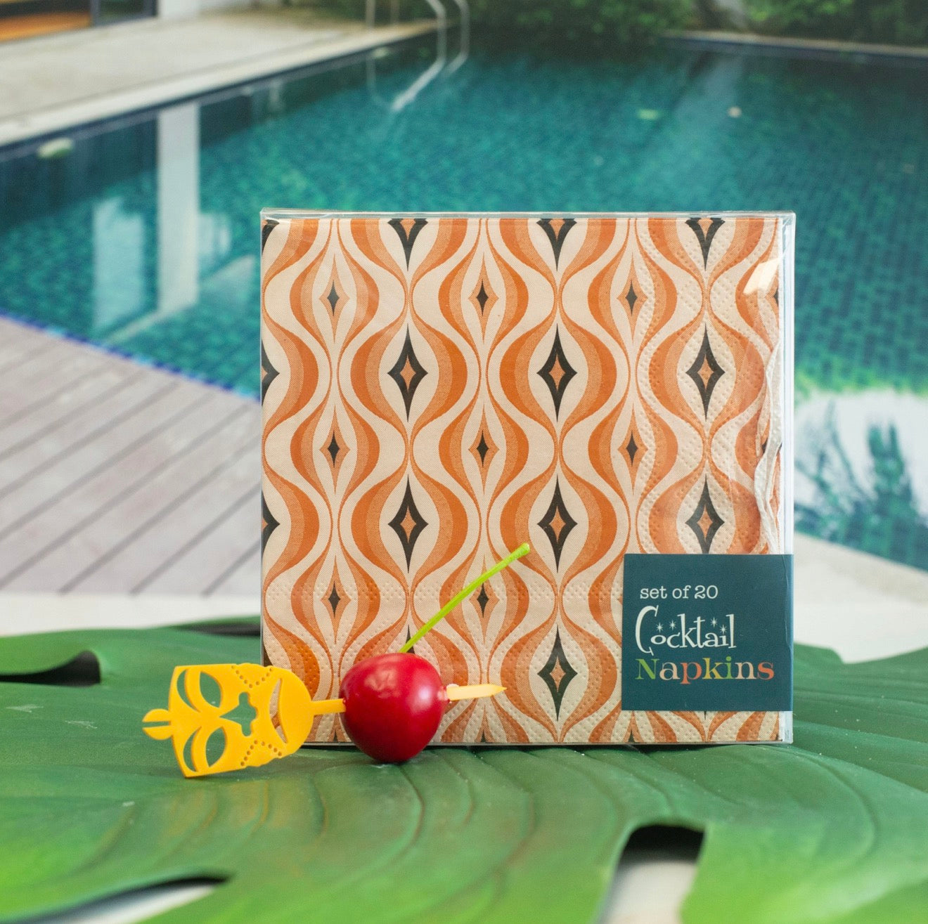 Retro orange cocktail napkins styled poolside with cherry garnish and tropical cocktail pick