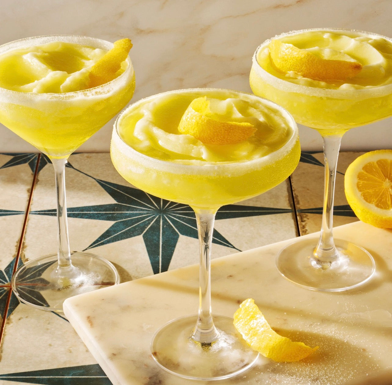 Frozen limoncello cocktails in coupe glasses with lemon garnish made with Noble Mick’s cocktail mix