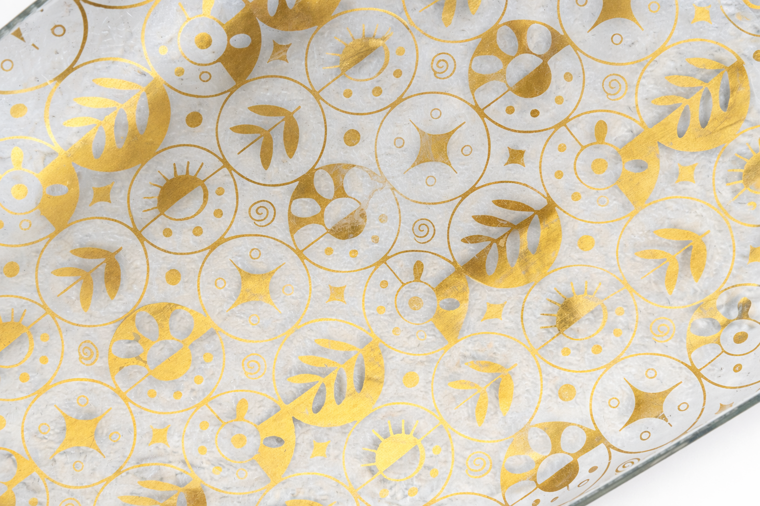 Close-up of 22K gold atomic sun and botanical medallion pattern on Georges Briard glass tray