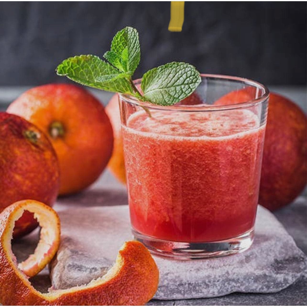 blood orange wine slushy cocktail displayed in a clear glass surrounded by freash oranges