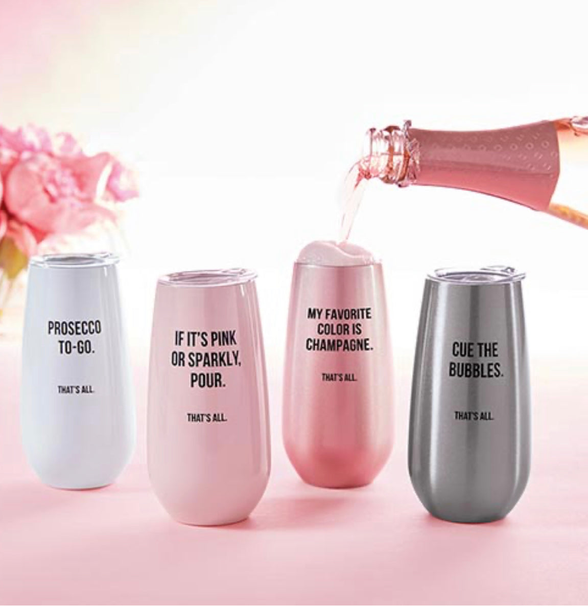 6 oz stainless steel champagne tumbler in a silver color with a plastic lid with words in black saying "Cue the bubbles. That's all." displayed with other tumblers of various colors and someone is pouring champagne into one of the tumblers