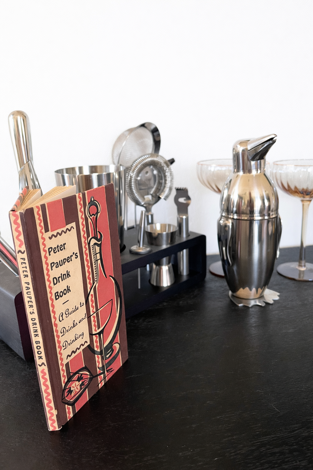 Vintage Peter Pauper Drink Book displayed on home bar with chrome cocktail shaker and coupe glasses
