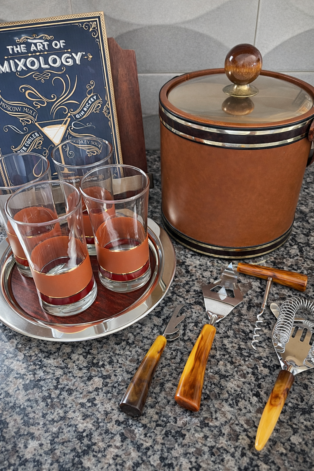 Mid century modern Bakelite barware tool set styled with vintage cocktail glasses and mixology book

