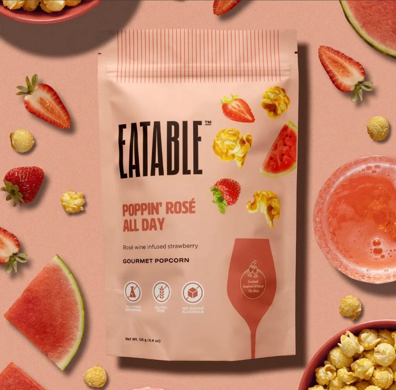 Flat lay of Poppin Rosé All Day popcorn bag with strawberries, watermelon slices, rosé drink, and popcorn
