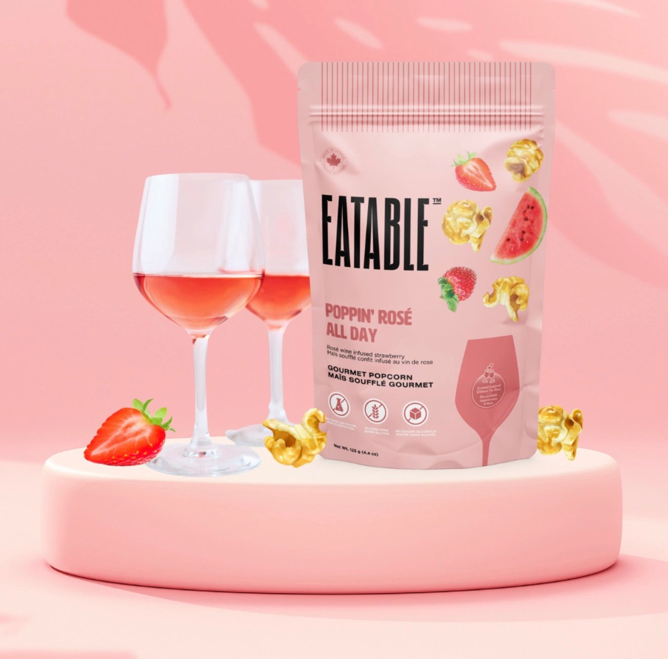 Eatable Poppin Rosé All Day popcorn bag displayed beside rosé wine glasses on pink backdrop