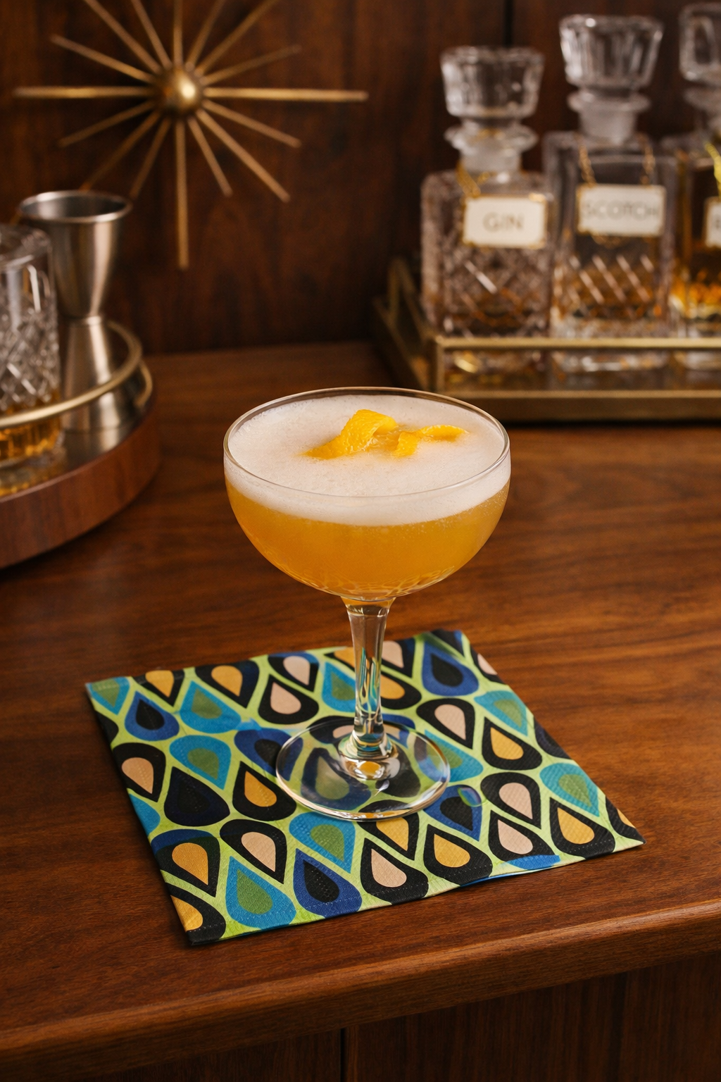 Mid century modern cocktail napkin styled on walnut bar with coupe cocktail and vintage glass decanters