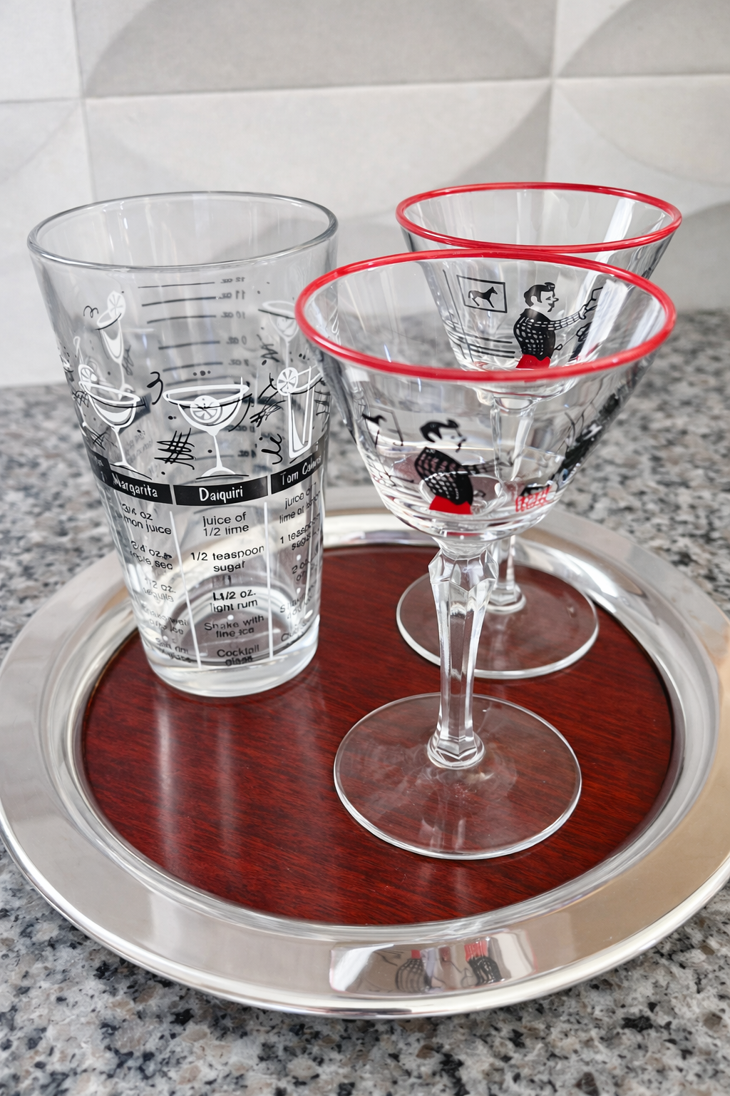 Retro cocktail mixing glass displayed with vintage martini glasses on tray in home bar setting with granite countertop.