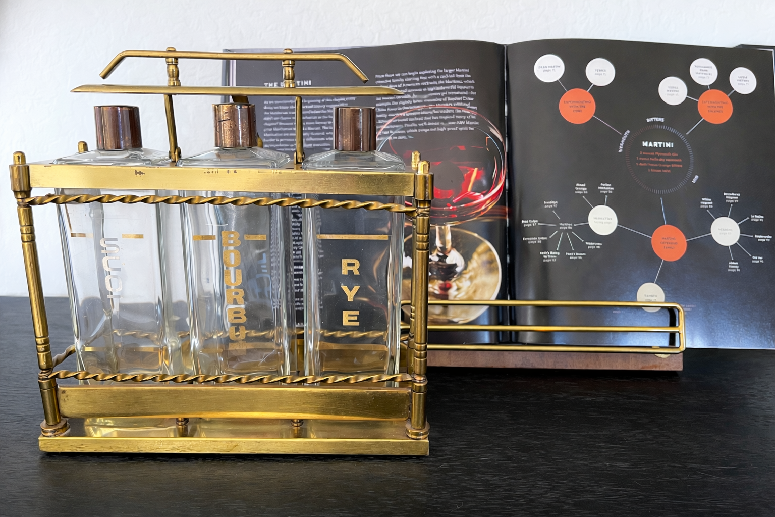 Vintage brass liquor decanter set styled beside open cocktail recipe book