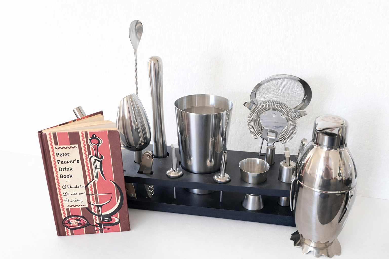 Vintage Peter Pauper cocktail book styled next to stainless steel bar tools and shaker