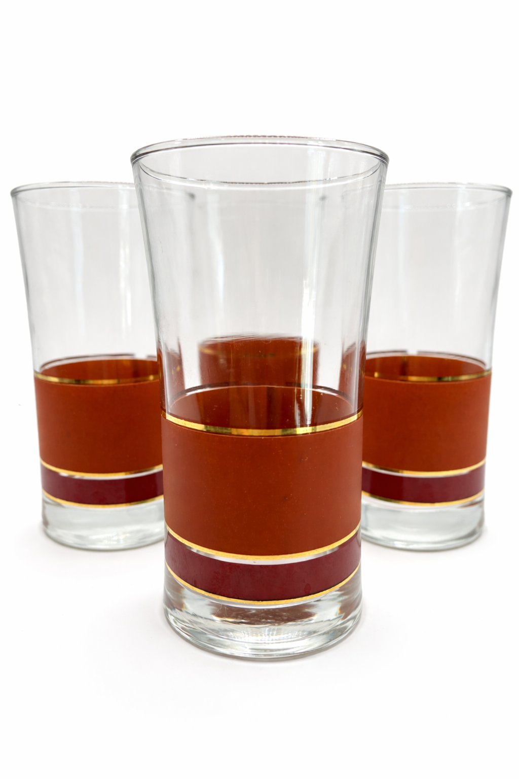 Set of three vintage mid-century modern highball glasses featuring brown and burgundy bands with gold trim on a white background