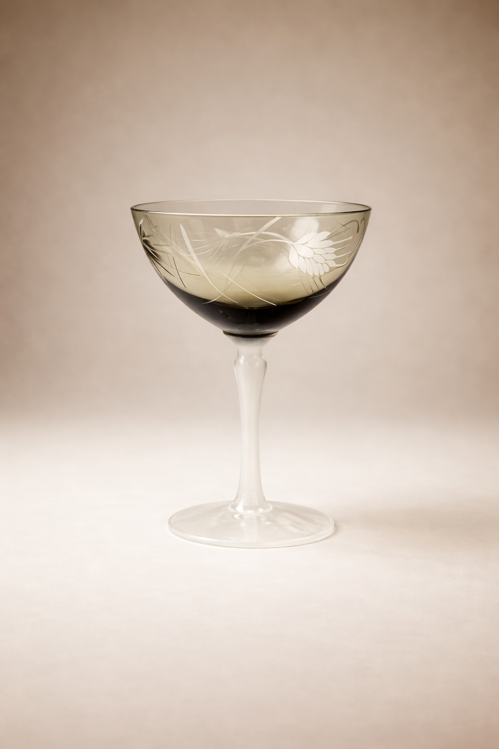 Single vintage coupe glass featuring a smoked bowl, white opaline stem, and delicate etched floral pattern on a warm neutral background
