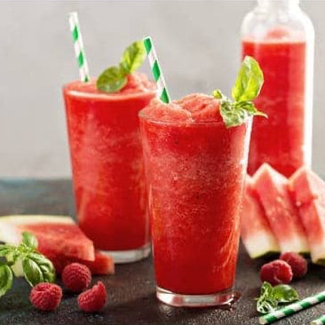 Two glasses of watermelon wine slushy on a wood table with slices of watermelon 