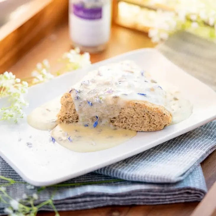 a scone on a white plate with a glaze poured over it that is sprinkled with the french lavender sugar