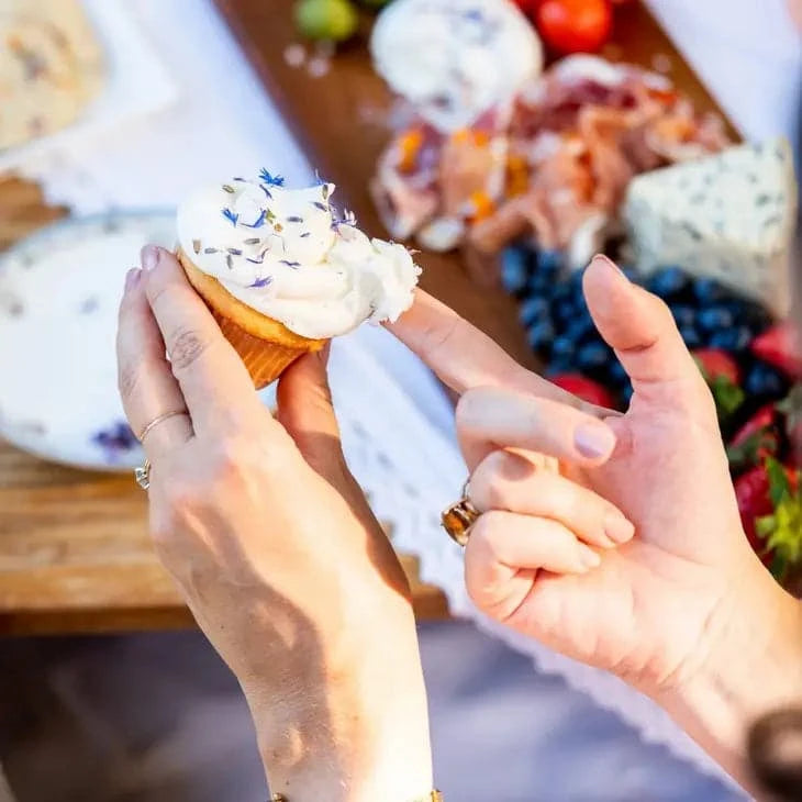 ladies hands holding a cupcake with one sugar scooping at the frosting that has been sprinkled with the french lavender finishing sugar