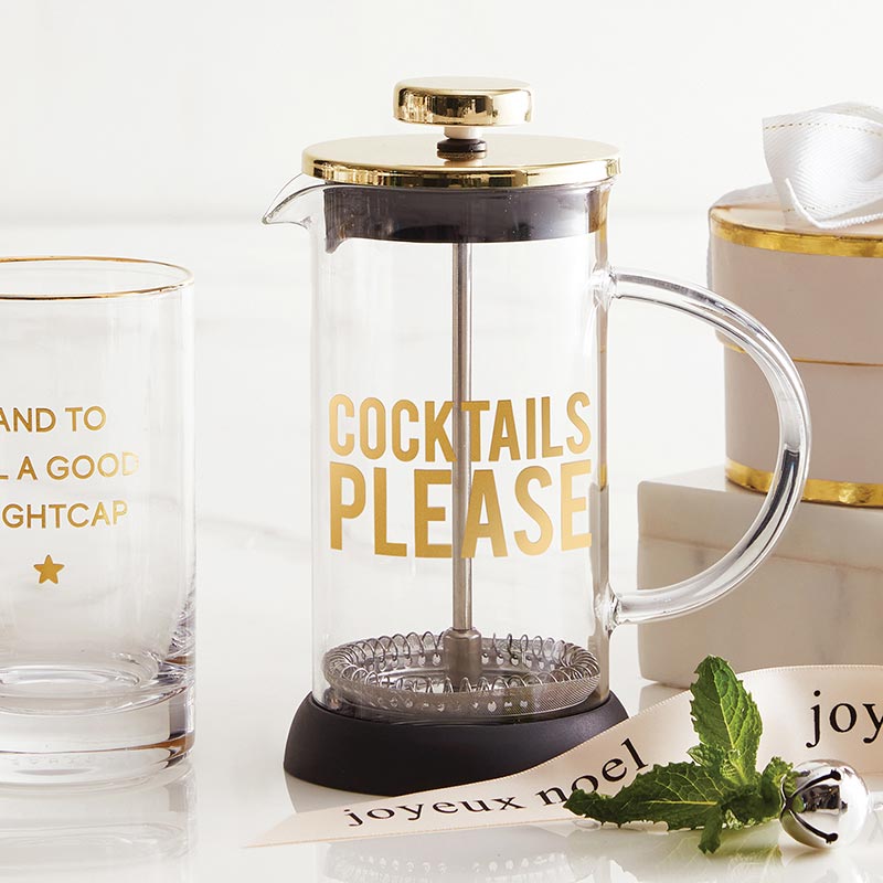 clear cocktail press featuring a gold lid and gold letters that say "cocktails please" displayed with a holiday double old fashioned glass and Christmas ribbon
