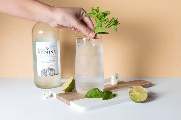 tall glass of mojito with limes and frsh mint sitting on a wood and marble cutting board