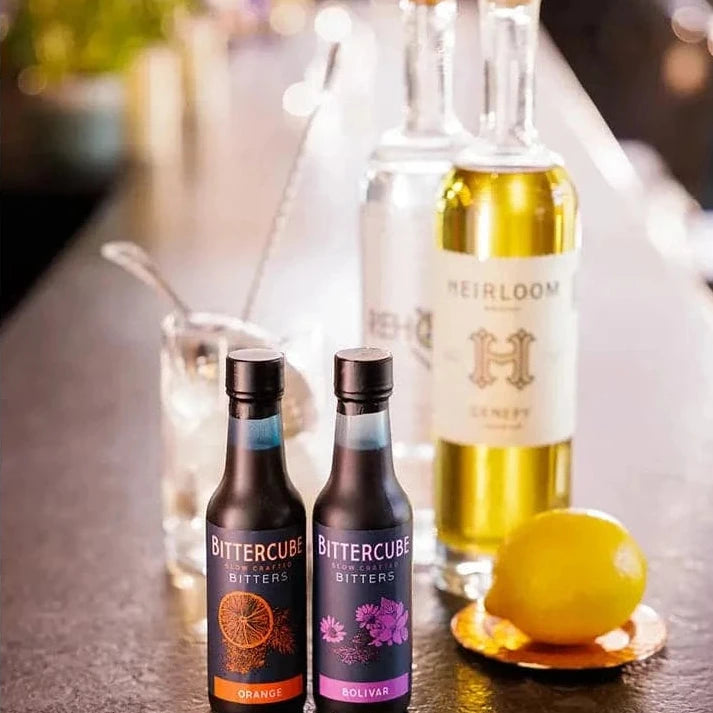 Bottles or orange and bolivar bitters displayed in front of a bottle of spirits with a lemon 