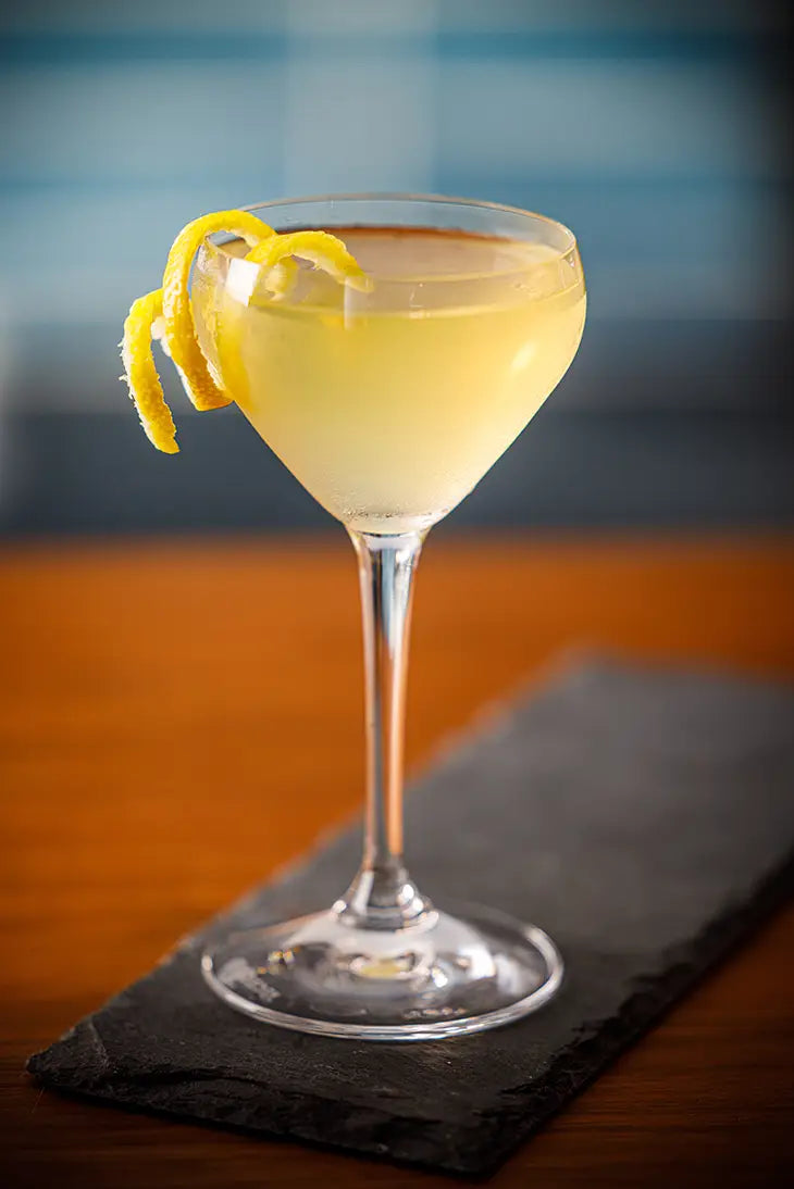 golden cocktail in a martini glass with a spiraled lemon peel garnishing the rim