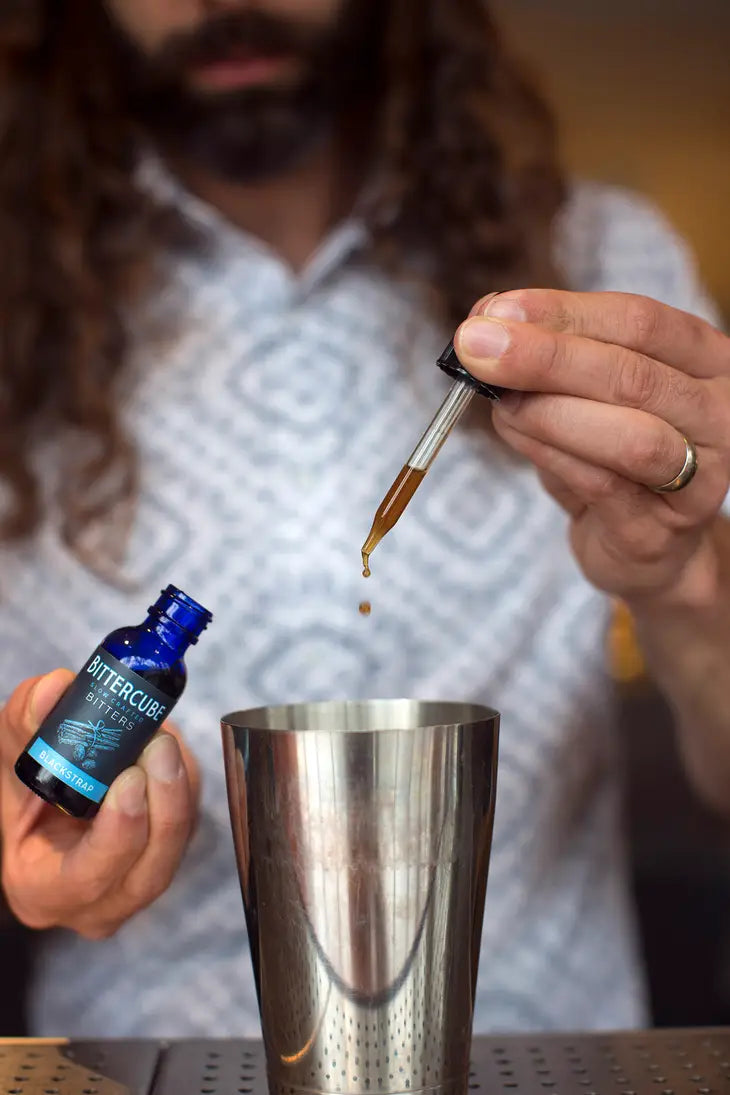 a man using a dropper to add bitters into a cocktail shaker
