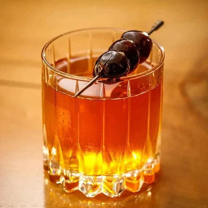 Glass of amber-colored cocktail with cherries on a wooden surface